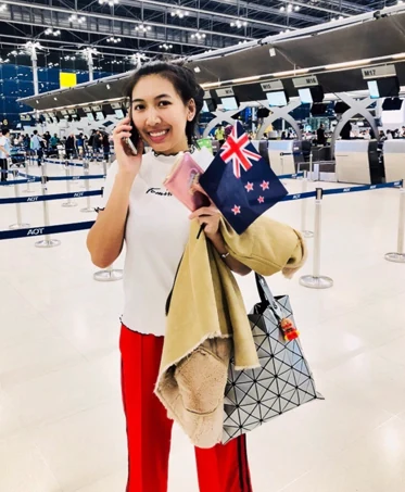 นักเรียนหญิงถือธงชาตินิวซีแลนด์ที่เคาน์เตอร์เช็กอินสนามบิน