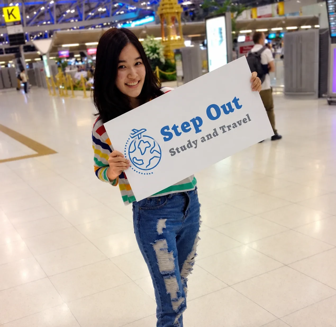 นักเรียนหญิงถือป้าย Step Out Study and Travel ที่สนามบินก่อนออกเดินทาง