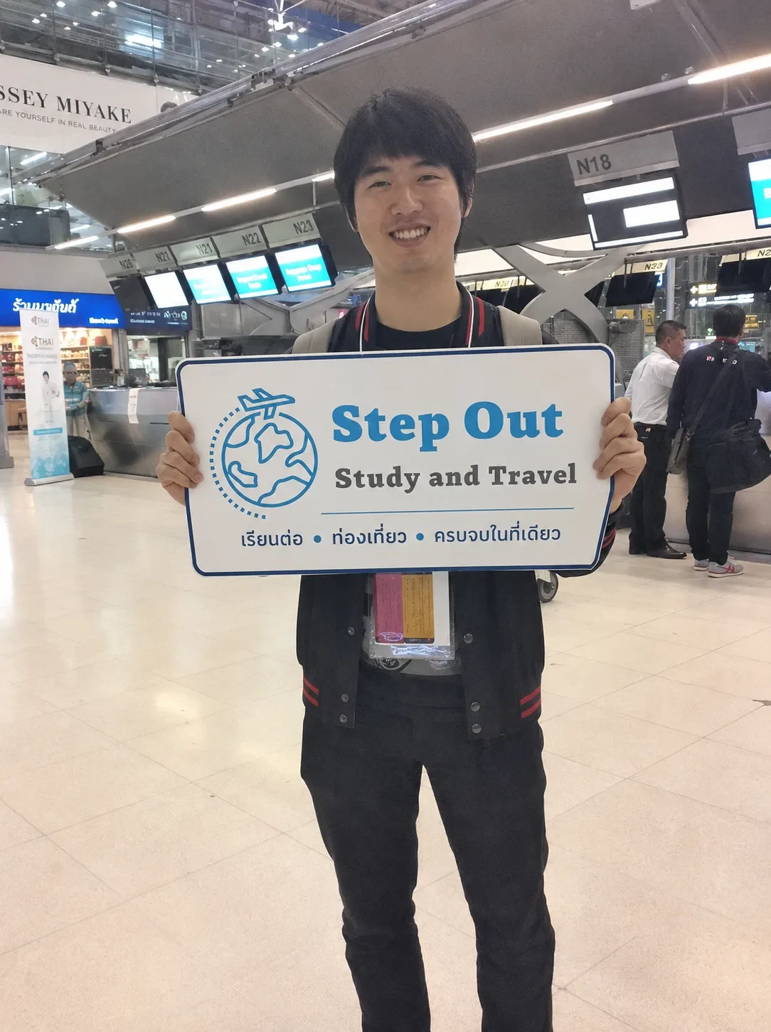 นักเรียนชายถือป้าย Step Out Study and Travel เรียนต่อ ท่องเที่ยว ครบจบในที่เดียว