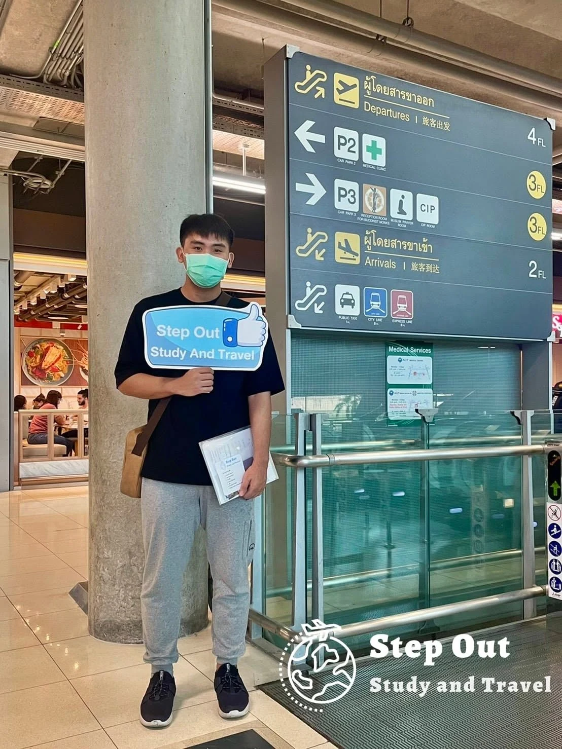 นักเรียนชายถือป้าย Step Out Study and Travel ที่จุดผู้โดยสารขาออก